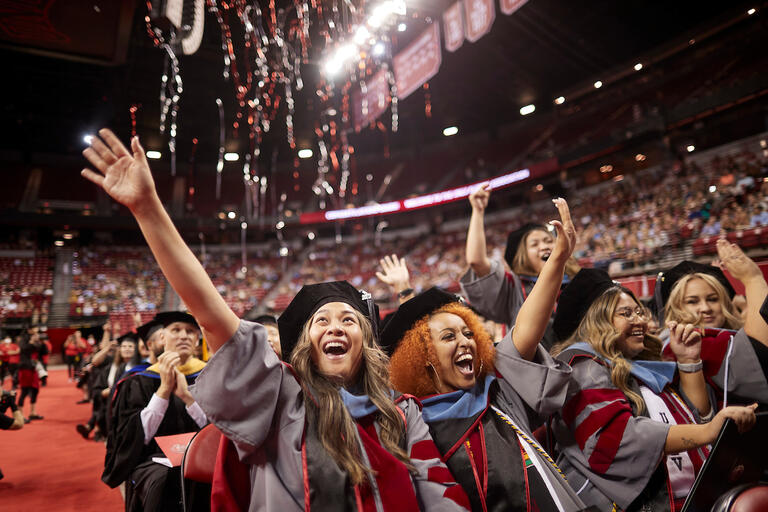 Doctoral students cheering during commencement as confetti falls from the ceiling.